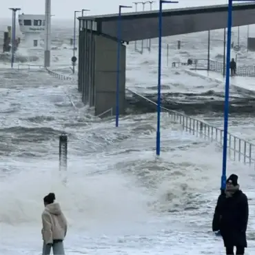 Hohe Sturmflutwellen überspülen die Hafenmole in Dagebüll. Menschen beobachten die aufgewühlte Nordsee bei stürmischem Wetter.