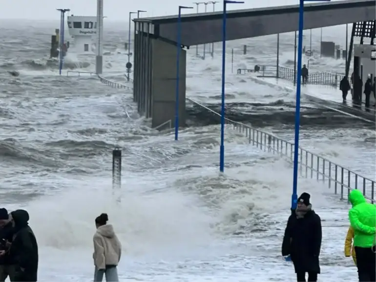 Hohe Sturmflutwellen überspülen die Hafenmole in Dagebüll. Menschen beobachten die aufgewühlte Nordsee bei stürmischem Wetter.