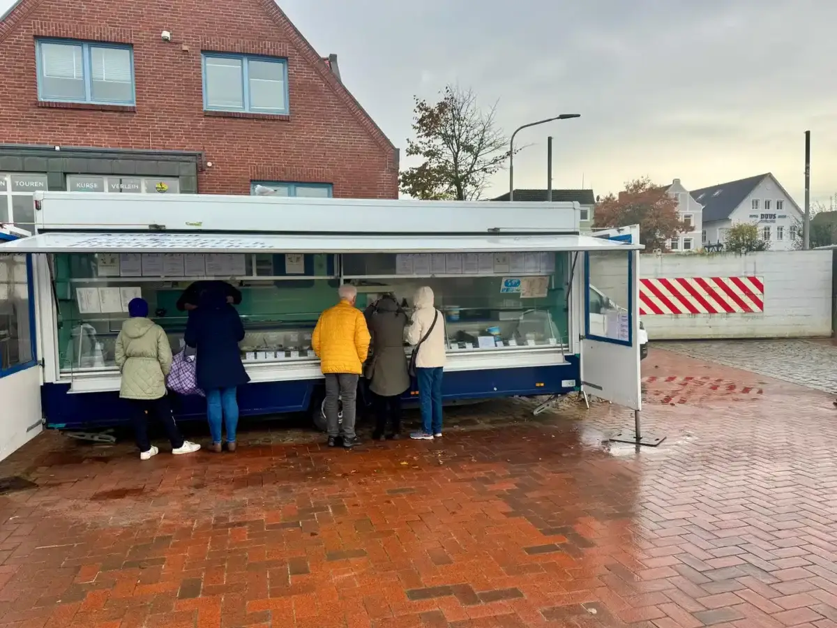 Kunden stehen bei Michael „Michi“ Denkers Fischwagen am Wyker Hafen auf Föhr. Im Hintergrund ist die wegen der Sturmflutgefahr geschlossene Hafenstöpe zu sehen.