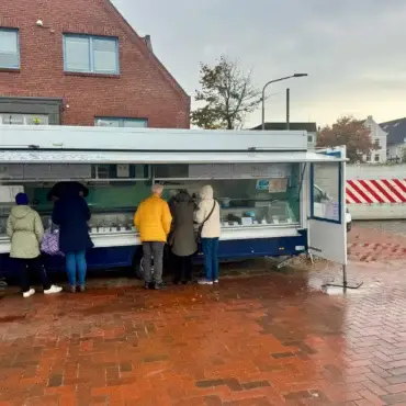 Kunden stehen bei Michael „Michi“ Denkers Fischwagen am Wyker Hafen auf Föhr. Im Hintergrund ist die wegen der Sturmflutgefahr geschlossene Hafenstöpe zu sehen.