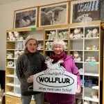 Gaby Brandt und ihr Mann Klaus halten im Wollflur in Wyk auf Föhr das Geschäftsschild mit der Aufschrift „Wollflur – Alles rund ums Schaf“.
