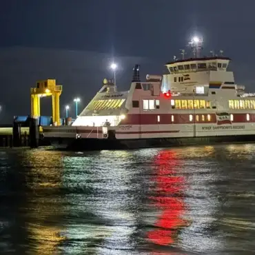 Die beleuchtete W.D.R.-Fähre Uthlande liegt am Samstagabend an der Mole in Dagebüll. Die Lichter spiegeln sich im bewegten Wasser.